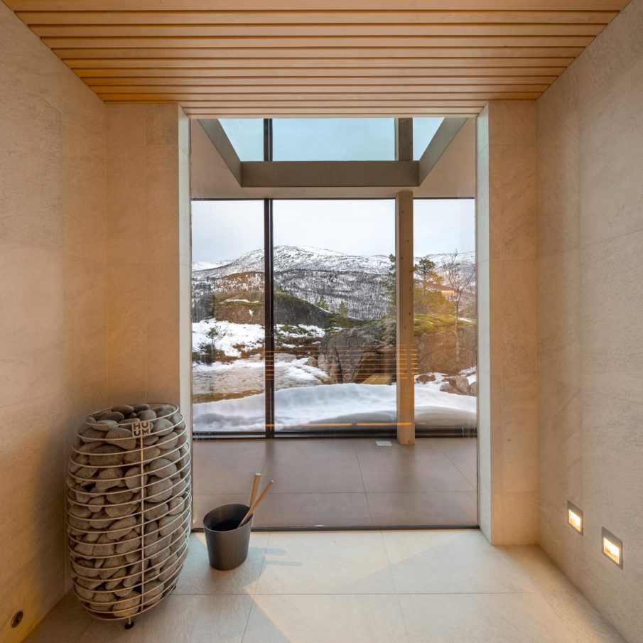 A room inside a cabin facing some large windows on the opposite side, with the mountain as a view.