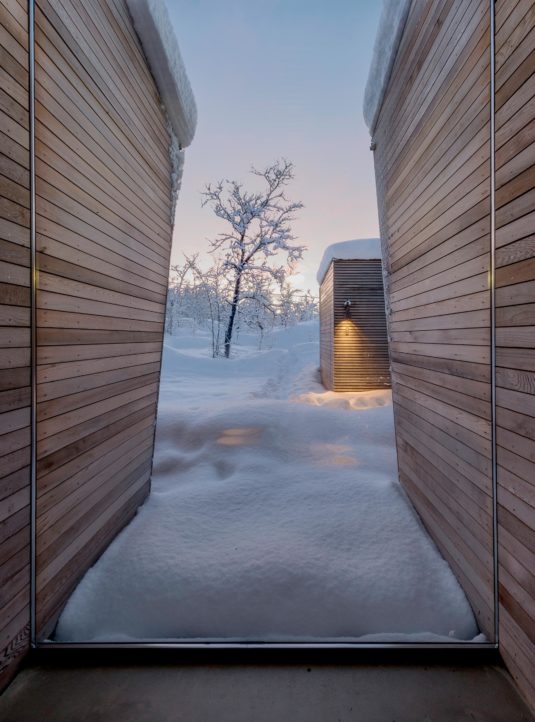 A large window in a cabin overlooking a wooden structure and snow as far as the eye can see.