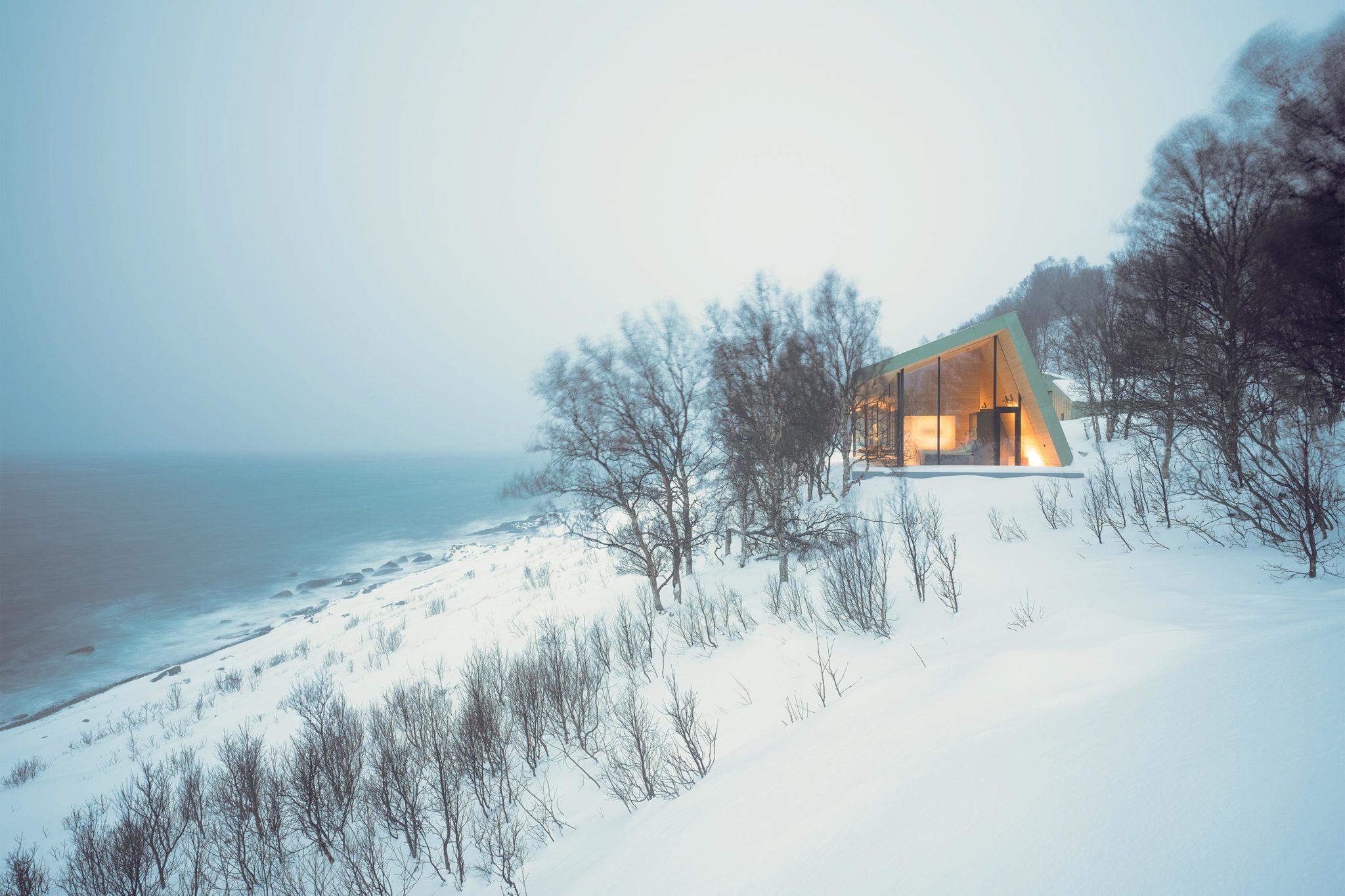 A cozy, cool cabin nestled in the mountain wall during winter with a view towards the sea.
