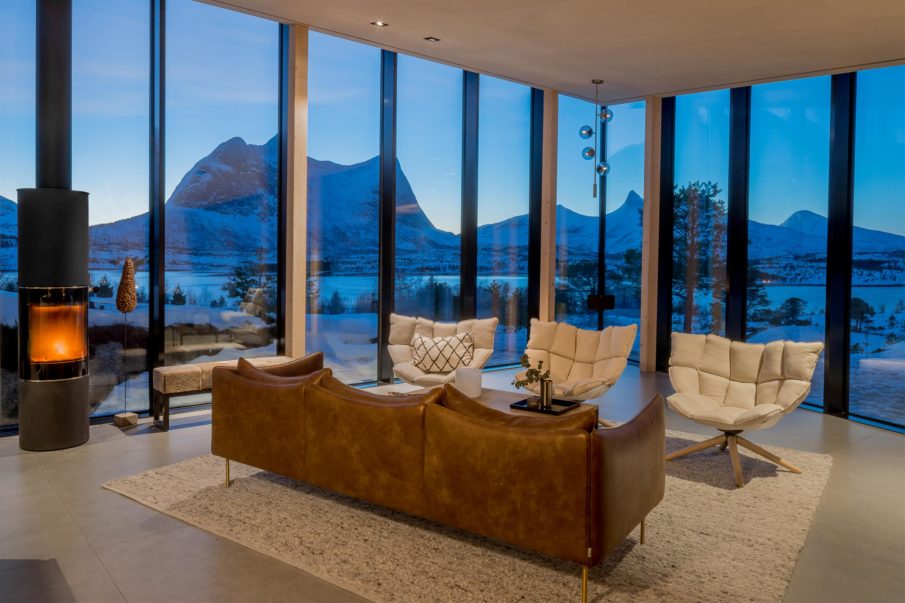 A living room with designer furniture and a fireplace, framed by large windows showcasing the view.