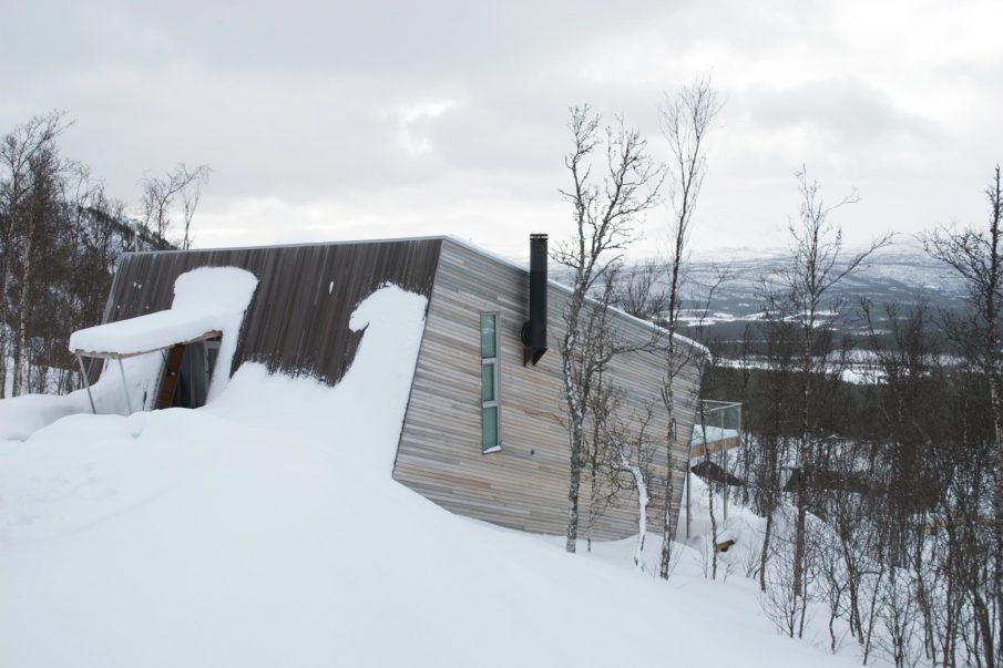 A snow-covered cabin nestled at an angle in the midst of the forest.